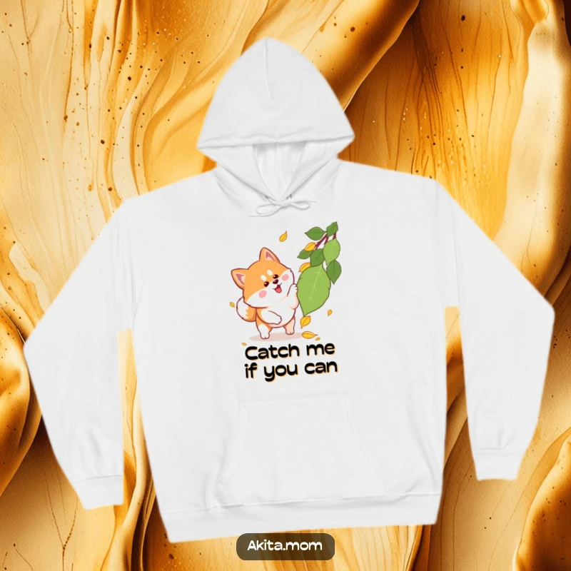 Funny Kawaii Akita hoodie depicting a cute dog with perky ears enthusiastically pouncing towards a falling autumn leaf, full of playful energy.